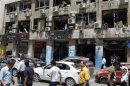 People walk on a street lined with a damaged building and destroyed cars after a blast at Marjeh Square in Damascus