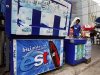 Man carries a bag with ice past a cooler with an advertisement for est sodas in Bangkok
