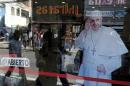 Pedestrians are reflected in a shop window which shows an image of Pope Francis in La Paz