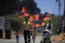 Members of a family walk on a street as flames rise after an explosion at the Amuay refinery near Punto Fijo, Venezuela, Sunday, Aug. 26, 2012. Venezuelans who live next to the country's biggest oil refinery said they smelled a strong odor of sulfur hours before a gas leak ignited in an explosion on Saturday that killed at least 39 people and injured more than 80. (AP Photo/Ariana Cubillos)