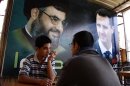 FILE - In this May 9, 2009 file photo, two Syrian men sit at a coffee shop under a big poster showing Syrian President Bashar Assad, right, and Hezbollah leader Sheik Hassan Nassrallah, left, in Damascus, Syria. U.S. officials said Israel launched a rare airstrike inside Syria on Wednesday. The target was a convoy believed to be carrying anti-aircraft weapons bound for Hezbollah, the powerful Lebanese militant group allied with Syria and Iran. The Israeli airstrike comes at a particularly sensitive and vulnerable time for Hezbollah in Lebanon. Despite its formidable weapons arsenal and political clout in the country, the group's credibility and maneuvering space has been significantly reduced in the past few years, largely because of the war in neighboring Syria but also because of unprecedented challenges at home. (AP Photo/Ola Rifai, File)