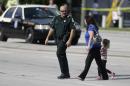An Orange County Sheriff's deputy, left, escorts a mother and her child across a street after a vehicle crashed into a day care center, Wednesday, April 9, 2014, in Winter Park, Fla. At least 15 people were injured, including children. (AP Photo/John Raoux)
