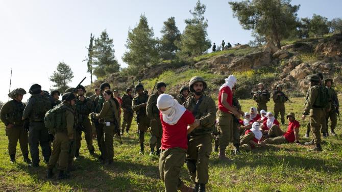 Israeli soldiers detain soldiers in red t-shirts, playing the role of Palestinian rioters, during a drill near the West Bank city of Hebron on March 1, 2015, organized by the Israeli army to simulate dispersing of riots and crowd control