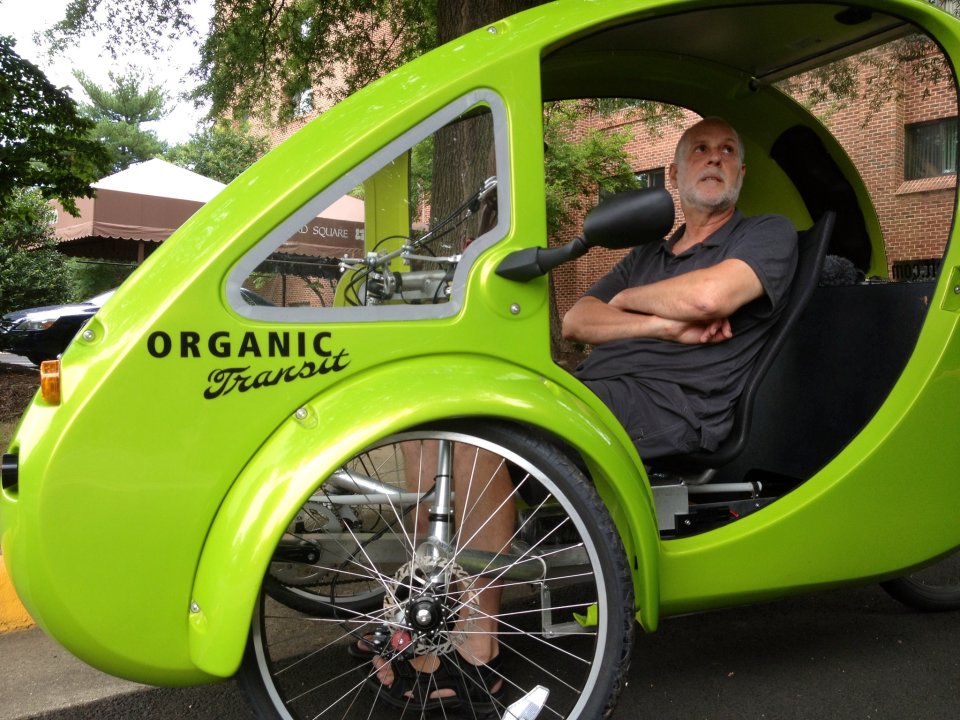 This photo taken July 24, 2013 shows ELF bike owner Mark Stewart describeing the features of his bike during a rest stop in Reston, Va. It’s the closest thing yet to Fred Flintstone’s footmobile _ only with solar panels and a futuristic shape. It’s an “Organic Transit Vehicle,” a car-bicycle blend also known as an ELF bike, and 65-year-old family therapist Mark Stewart is taking it on a 1,200-mile journey along the East Coast Greenway, a bike and pedestrian trail that runs from Florida to Canada. (AP Photo/Valerie Bonk)