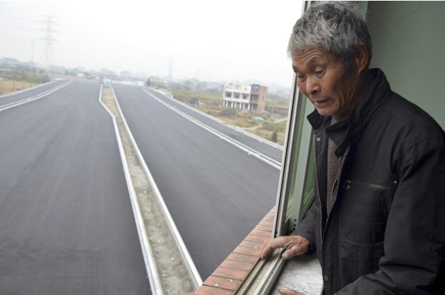 An old man looks down from his house which stands alone in the middle of a newly built road in Wenling, Zhejiang province