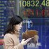 A woman walks by an electronic stock board of a securities firm in Tokyo, Friday, Jan. 25, 2013.  Japan’s benchmark stock index jumped about 2 percent Friday after the country’s currency continued to slide against the dollar. (AP Photo/Koji Sasahara)