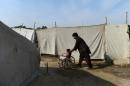 An Afghan man pushes a disabled child in a wheelchair outside a refugee tent during a polio immunisation campaign in Jalalabad in Nangarhar Province on February 24, 2014