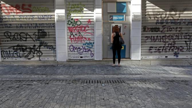 A woman withdraws money at an ATM outside a National Bank branch in Athens