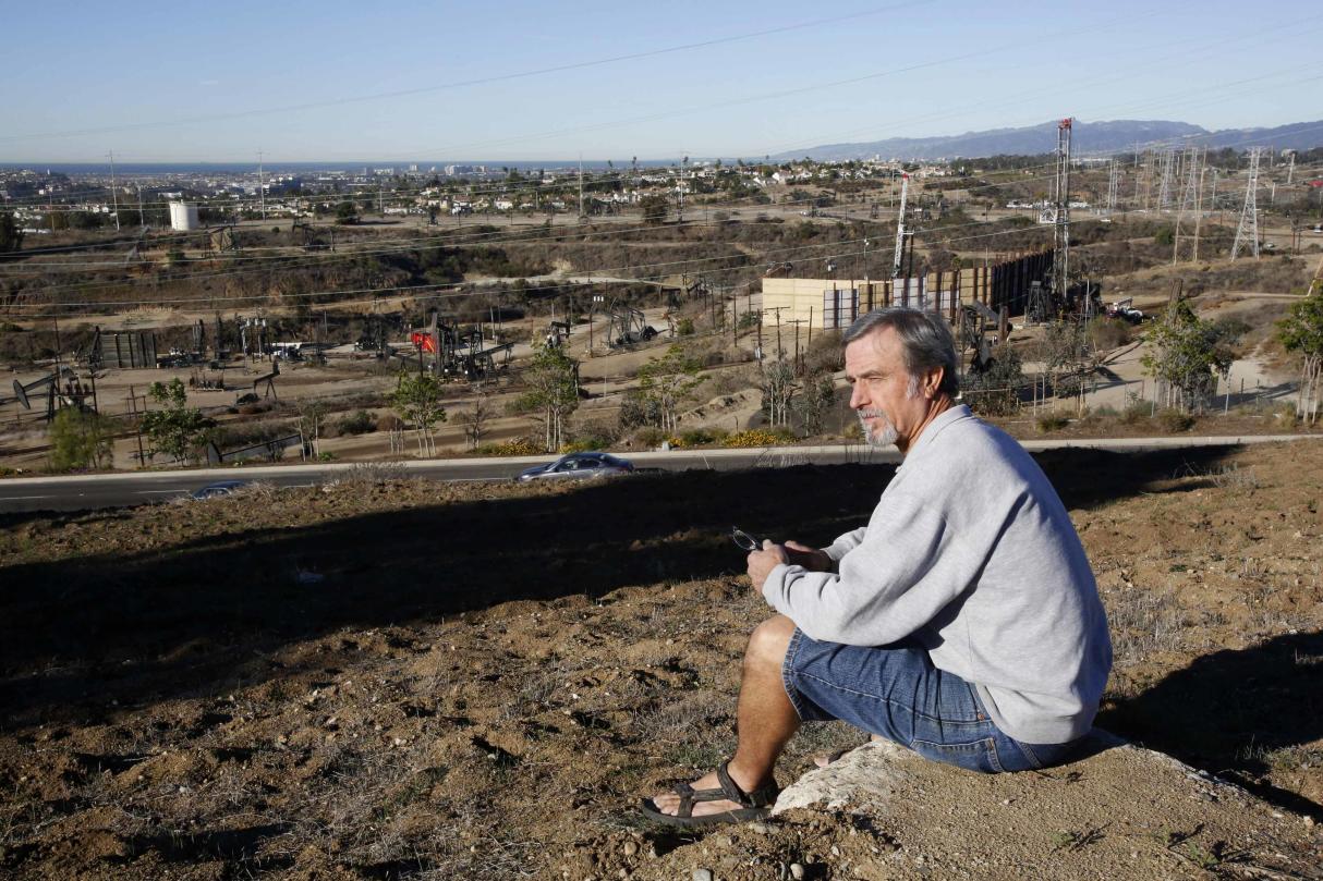 Homeowner Gary Gless sits on a hill in his neighborhood overlooking drilling wells in Los Angeles