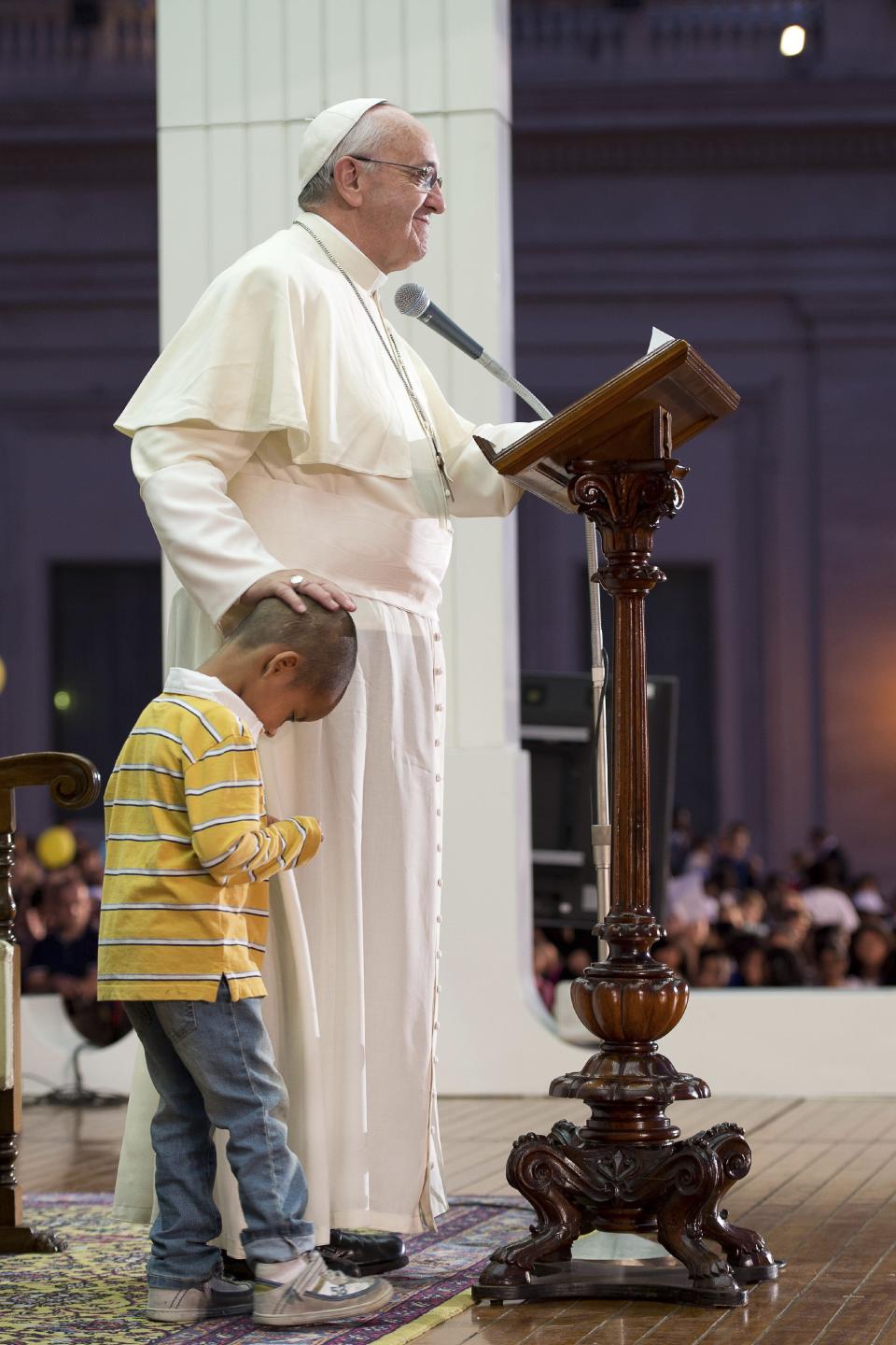 In this Saturday, Oct. 26, 2013 photo provided by the Vatican newspaper L'Osservatore Romano, Pope Francis touches a boy's head, no name available, as he delivers his speech during an audience with families in St. Peter's Square gathered for the Pontifical Council for the Familyís plenary assembly, at the Vatican. A young boy, part of a group of children sitting around the stage where the pontiff was delivering his message to families, played around Pope Francis as he continued delivering his speech, occasionally patting the boy's head. (AP Photo/L'Osservatore Romano)