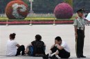 Visitors take a rest next to paramilitary policeman standing guard at Tiananmen Square in Beijing