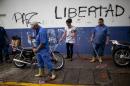 Workers clean the street from debris left over from yesterday's clashes between anti government protestors and police in Caracas, Venezuela, Thursday, Feb. 20, 2014. The graffiti on the wall reads in Spanish "Peace and Liberty". Violence is heating up in Venezuela as an opposition leader Leopoldo Lopez, faces criminal charges for organizing a rally that set off a deadly week of turmoil in anti-government protests in Caracas and other cities where demonstrators and government forces clashed leaving several dead and scores of wounded. (AP Photo/Rodrigo Abd)