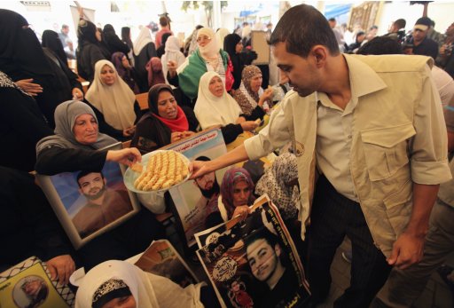 A man hands out sweets to Palestinian women holding pictures of their jailed sons during a demonstration calling for their release at the International Red Cross headquarters in Gaza City