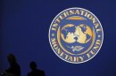Visitors are silhouetted against the logo of the International Monetary Fund (IMF) in Tokyo