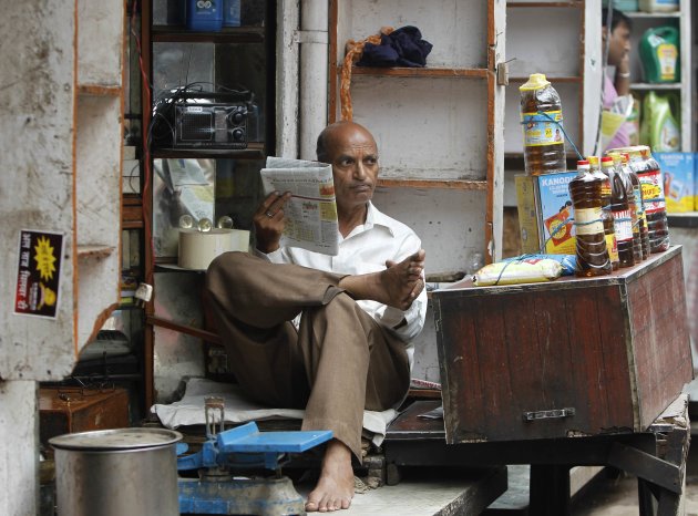 A shopkeeper selling cooking oil reads a newspaper inside his shop at a market in the old quarters of Delhi
