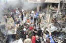 A crowd gathers in front of a building and car damaged after a bomb explosion in the Mezzeh 86 area in Damascus