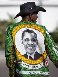 A member of the brass band that will welcome U.S. President Barack Obama walks on the road next to State House, wearing a shirt with the face of Obama, ahead of the meeting with Tanzanian President Jakaya Kikwete, at State House in Dar es Salaam, Tanzania Monday, July 1, 2013. The Democratic president was to fly Monday into Dar es Salaam, Tanzania, the last stop on a weeklong tour of Africa that wraps up Tuesday, while his Republican predecessor coincidentally also plans to be there for a conference on African women organized by the George W. Bush Institute. (AP Photo/Ben Curtis)