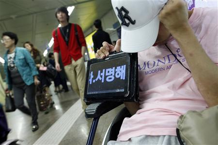 A disabled man on a wheelchair holds an iPad that shows the demands of the disabled in Seoul