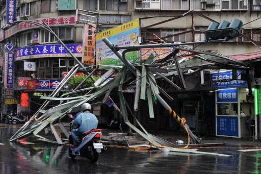 A motorcycle drives past a damaged tin roof and traffic signs in Taipei, on July 13, 2013