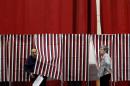 In this Jan. 10, 2012, file photo, ballot inspector Connie Bell, right, holds open a curtain on a voting booth during voting in the first-in-the-nation presidential primary at Memorial High School in Manchester, N.H. It's been 100 years since New Hampshire held its first presidential primary, and it seems like some of the current candidates have been hanging around for nearly that long.(AP Photo/Matt Rourke, File)