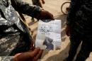 An Iraqi soldier shows a pamphlet which reads "Wearing beards is compulsory, shaving is prohibited" along a street of the town of al-Shura
