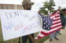 Joseph Offutt, left, and Raheem Peters hold a sign and a U.S. flag across the street from the Curtis Culwell Center, Tuesday, May 5, 2015, in Garland, Texas. A man, whose social media presence was being scrutinized by federal authorities, was one of two suspects killed in the Sunday shooting at this location that hosted a cartoon contest featuring images of the Muslim Prophet Muhammad. The Islamic State group on Tuesday claimed responsibility for the attack. (AP Photo/LM Otero)
