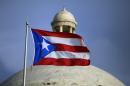 In this Wednesday, July 29, 2015 photo, the Puerto Rican flag flies in front of Puerto Rico's Capitol as in San Juan, Puerto Rico. Nearly 10 years into a deep economic slump, Puerto Rico is no closer to pulling out, and, in fact, is poised to plummet further. The unemployment rate is above 12 percent and tens of thousands have migrated out of the island. (AP Photo/Ricardo Arduengo)
