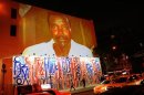 Passersby walk under a projection that is part of the non-profit organization Invisible Children's "Kony 2012" viral video campaign, in New York