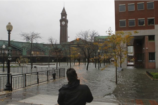 A person looks at water from the Hudson River spilling over a wall flooding the street in front of the train station in Hoboken