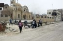 Residents walk near a damaged church as they are seen in Qusair to inspect their houses and collect their belongings