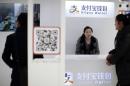 Sales assistant sits behind and under Alipay logos at a train station in Shanghai