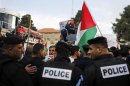 Palestinian policemen stand in front of demonstrators holding digitally manipulated placards depicting U.S President Obama during a protest in Ramallah