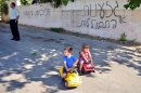 FILE - An Israeli-Arab man and children are seen on a street next to Hebrew graffiti that reads, "Racism or assimilation" and "Arabs out," in the village of Abu Ghosh near Jerusalem, June 18, 2013. In a land rife with religious tension, the village of Abu Ghosh has proven to be an exception, but that tranquility was briefly disturbed this week when Abu Ghosh became the latest victim in a wave of hate crimes that has plagued Israel, when unknown assailants slashed the tires of more than two dozen cars and sprayed anti-Arab graffiti. (AP Photo/Mahmoud Illean, File)