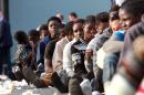 Migrants sit in line after disembarking upon their arrival in the port of Catania on the coast of Sicily on June 8, 2015