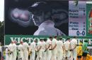 Australian teammates pause for a moment at the Sydney Cricket Ground as a photo of their teammate Phil Hughes appears on a screen during the opening ceremony for their cricket test match against India in Sydney, Tuesday, Jan. 6, 2015. Hughes died in Nov. 2014, after he was hit in the head with the ball while playing on the ground. (AP Photo/Rick Rycroft)