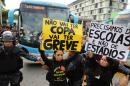 Demonstrators hold up signs that read in Portuguese "There won't be a Cup. There will be strikes," center, and "We need schools, not stadiums" as they walk in front of the bus carrying members of Brazil's national soccer team as it leaves a hotel for the Granja Comary training center, where the team will train and reside during the World Cup, in Rio de Janeiro, Brazil, Monday, May 26, 2014. Demonstrators are protesting the money being spent by the local government on the World Cup. (AP Photo/Leo Correa)