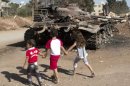 Tres niños pasan frente a un tanque destruido al norte de Siria