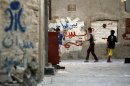 Bahraini children play in an alley spray-painted with anti-government graffiti in Malkiya, Bahrain, on Monday, Aug. 6, 2012. At left above the words "Martyrs Square," is a painted image of the since-demolished monument that stood at the site of huge Spring 2011 pro-democracy protests. Back wall graffiti includes "down Hamad," referring to Bahrain's king. (AP Photo/Hasan Jamali)