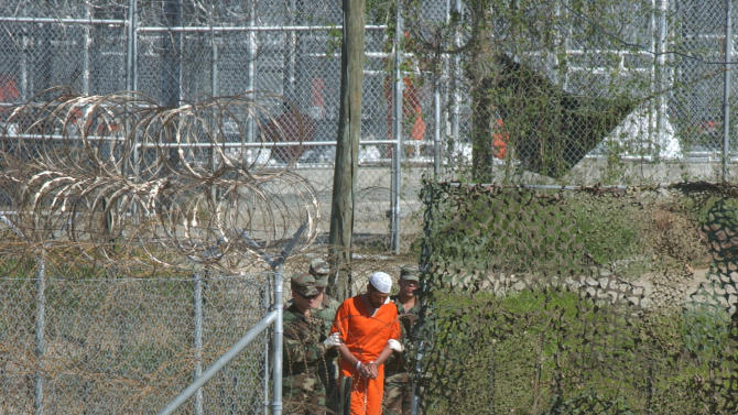 In this March 1, 2002 file photo, a detainee is escorted to interrogation by U.S. military guards at Camp X-Ray at Guantanamo Bay U.S. Naval Base, Cuba. The U.S. government announced Tuesday Dec. 30, 2014, that five men who were held for a dozen years without charge at the U.S. Navy base at Guantanamo Bay, Cuba, have been sent to the Central Asian nation of Kazakhstan for resettlement. (AP Photo/Andres Leighton, File)