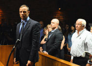 Olympian Oscar Pistorius, foreground, stands following his bail hearing, as his brother Carl, centre, and father Henke, right, look on, in Pretoria, South Africa, Tuesday, Feb. 19, 2013. Pistorius fired into the door of a small bathroom where his girlfriend was cowering after a shouting match on Valentine's Day, hitting her three times, a South African prosecutor said Tuesday as he charged the sports icon with premeditated murder. The magistrate ruled that Pistorius faces the harshest bail requirements available in South African law. He did not elaborate before a break was called in the session. (AP Photo-Masi Losi-Pretoria News) SOUTH AFRICA OUT