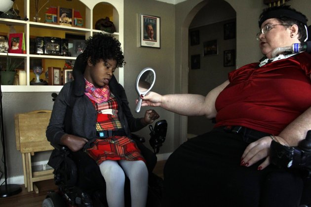 In this Nov. 14, 2012 photo, Carrie Ann Lucas, right, mother of four disabled adopted children, holds up a mirror for her daughter, Adrianne, 13, at their home in Windsor, Colo., before going on an outing. Carrie Ann Lucas herself uses a power wheelchair and is reliant on a ventilator due to a form of muscular dystrophy. In diverse and profound ways, the millions of Americans with disabilities have gained rights and opportunities since Congress passed landmark legislation on their behalf in 1990. Advocates say barriers and bias still abound, however, when it comes to one basic human right: To be a parent. (AP Photo/Brennan Linsley)