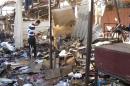 People stand among debris at the site of a bomb attack at a marketplace in Baghdad's Doura District