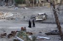 People walk past a destroyed car in a street lined with damaged buildings in Deir al-Zor