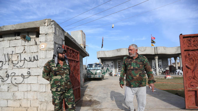 In this Saturday, Jan. 3, 2015 photo, Adnan Hassan, 59, right, and another Shiite militia member are seen outside a house they took over in Al-Rawashid a Sunni village outside the Iraqi city of Balad. 75 kilometers (45 miles) north of Baghdad, Iraq. He and his men last week helped Iraqi forces wrest the town from the hands of the Islamic State group. (AP Photo/Hadi Mizban)