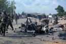 Military officers walk past the remains of a car after an explosion on July 23, 2014 in Kaduna, north of Nigeria