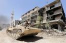 Syrian government troops drive past a damaged building in Mleiha, on the outskirts of Damascus, August 15, 2014