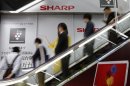 File photo shows shoppers on an escalator travelling past Sharp's advertisement board at an electronic shop in Tokyo