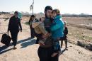 An Iraqi man carries his children near the town of Bartella as people return to their liberated neighbourhoods in eastern Mosul on January 7, 2017