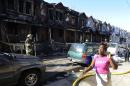 A woman cries as she walks past Philadelphia firefighters working on burned row homes on Saturday, July 5, 2014, in Philadelphia. A fast-moving fire in southwest Philadelphia early Saturday left four children dead and burned through a number of adjoining homes. (AP Photo/Michael Perez)