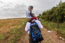A man carries a child on a dirt road towards the Serbia-Croatia border, near the western-Serbia town of Sid, on September 20, 2015